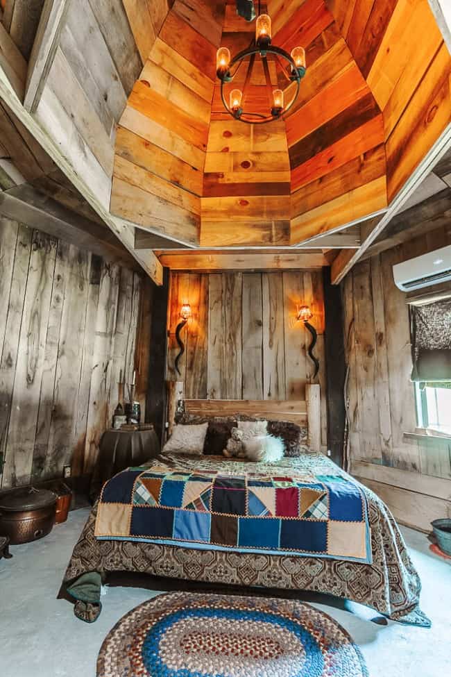 The Groundkeeper’s Hut bedroom with vaulted ceilings, a chandelier-style light, and multi-colored patchwork quilt bedding.